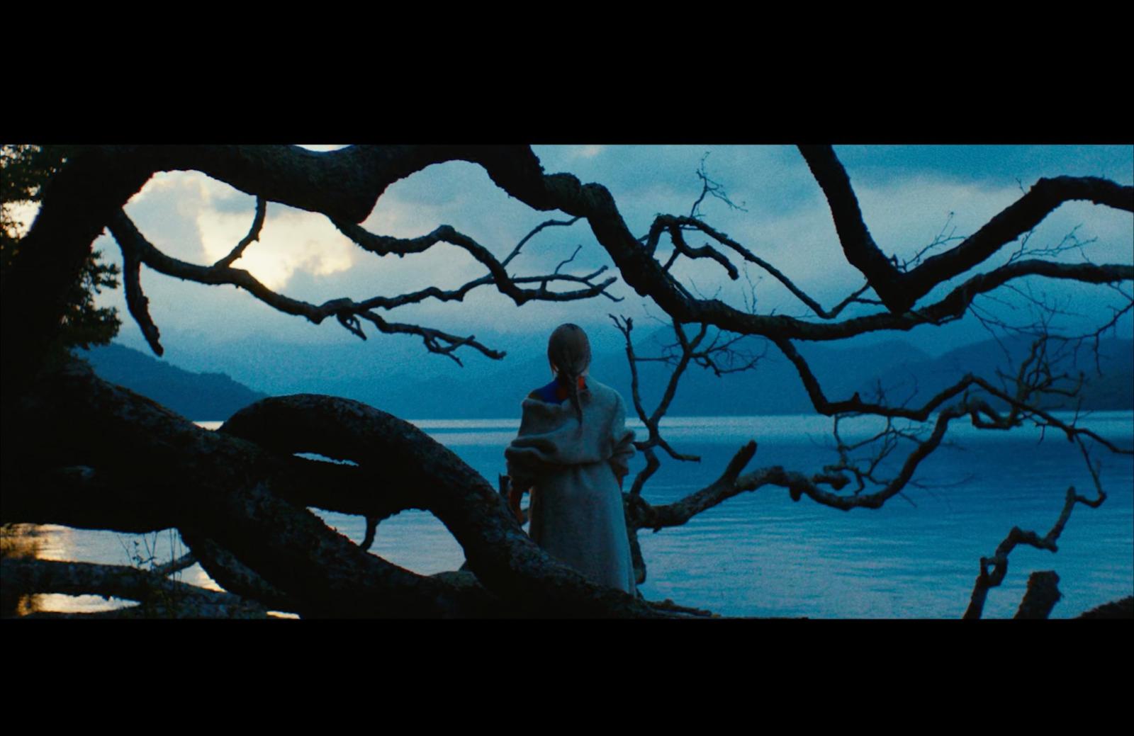 a woman standing next to a tree near a body of water