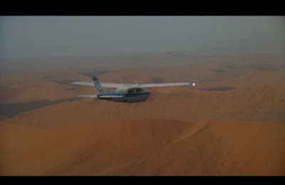 a small airplane flying over a desert landscape