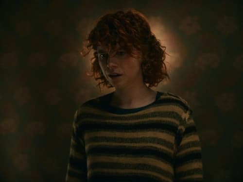 a woman with red hair standing in a dark room