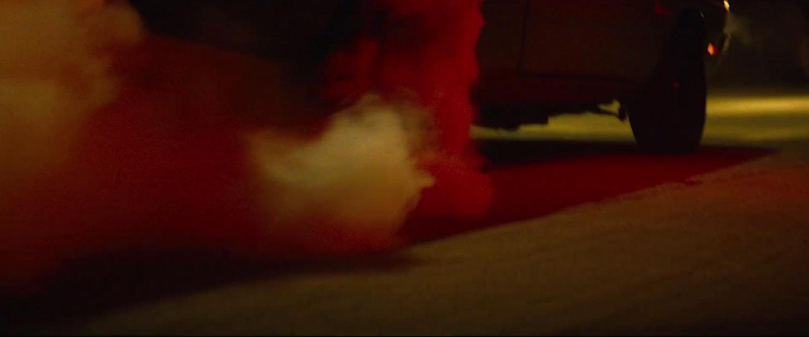 a red teddy bear sitting on the ground next to a car