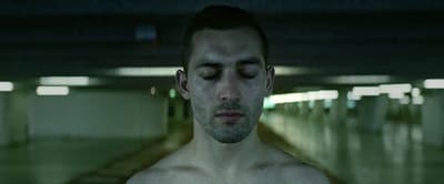 a shirtless man in a parking garage with his eyes closed