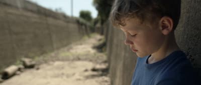 a young boy standing next to a cement wall