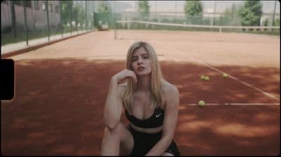 a woman sitting on a tennis court holding a tennis racket