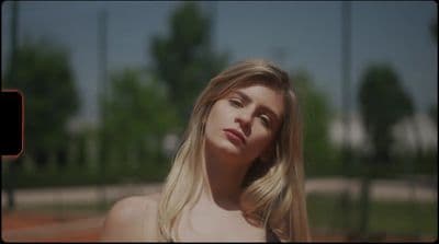 a woman with long blonde hair standing in front of a tennis court