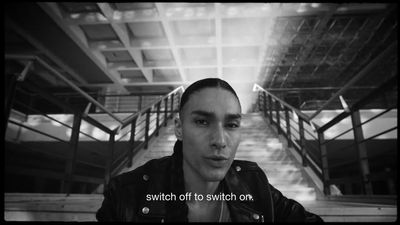 a man in a black jacket standing in front of a staircase