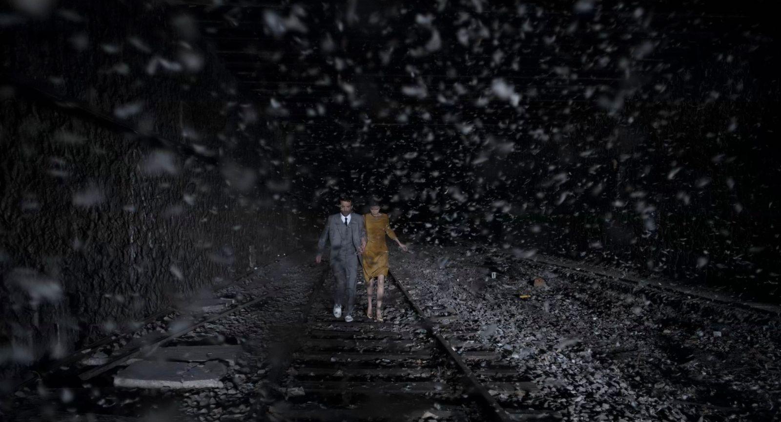 two people walking down a train track in the rain