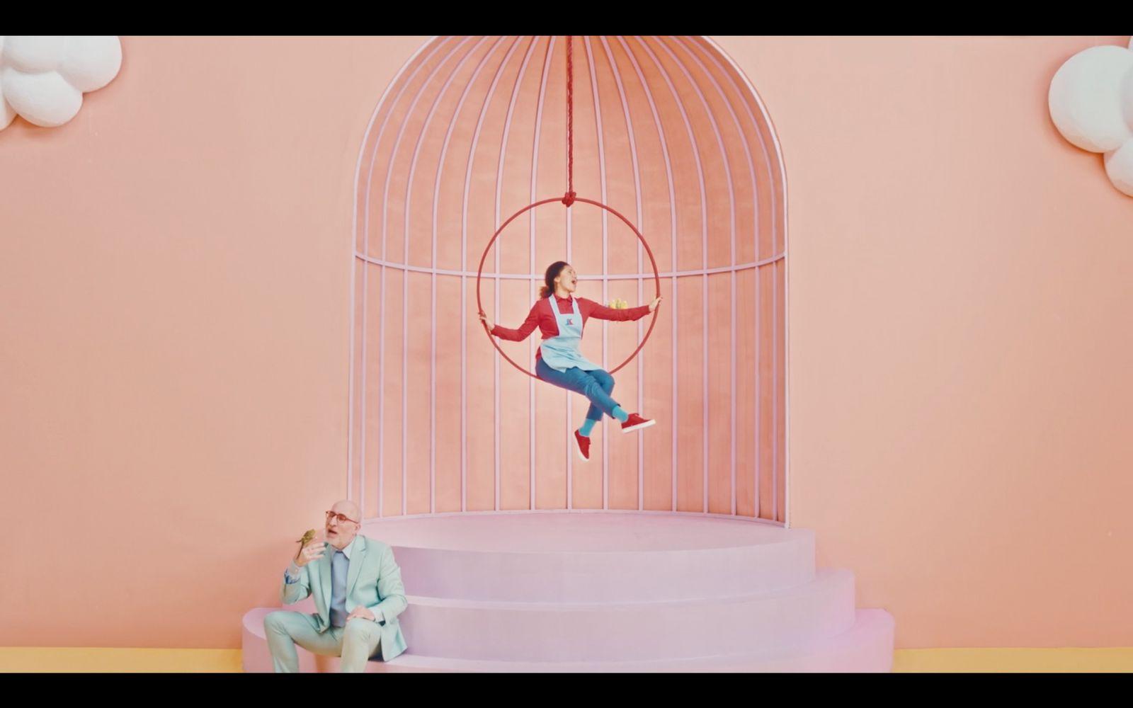 a man and a woman sitting on a chair in front of a birdcage