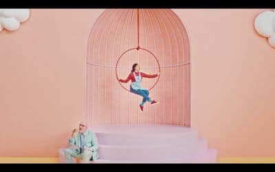 a man and a woman sitting on a chair in front of a birdcage