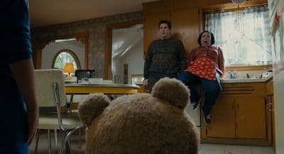 a man and a woman standing in a kitchen with a teddy bear