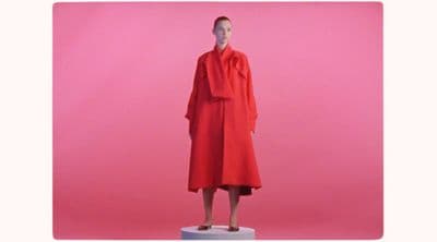 a mannequin dressed in a red coat stands in front of a pink background
