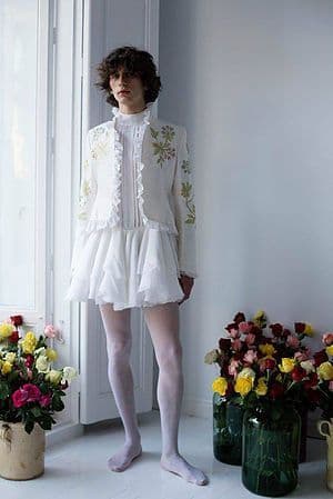 a woman standing in front of a window next to flowers