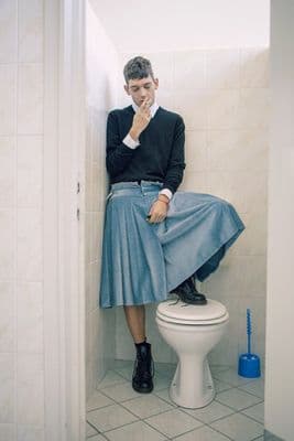 a man sitting on top of a toilet in a bathroom