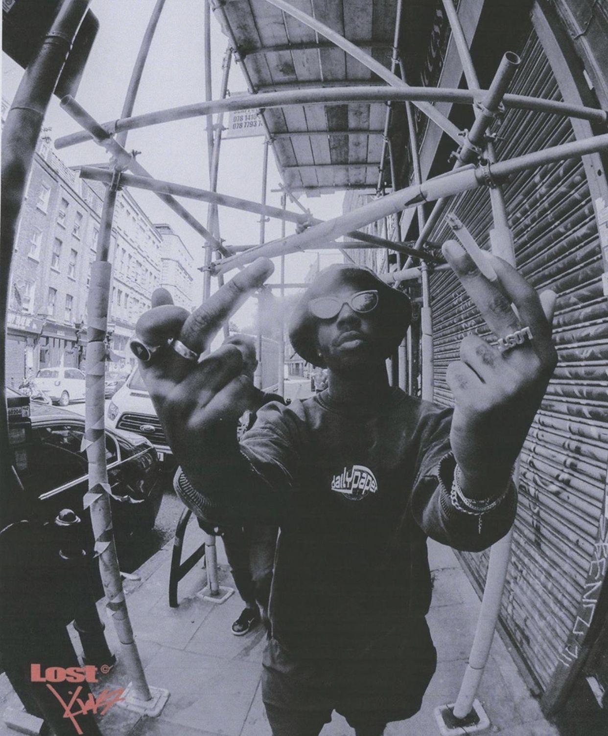 a man holding up his hands while standing in front of a building