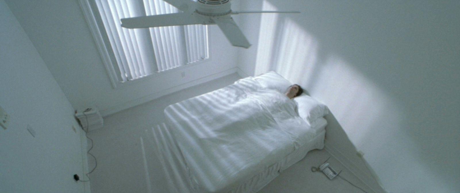a white bed sitting under a window next to a ceiling fan