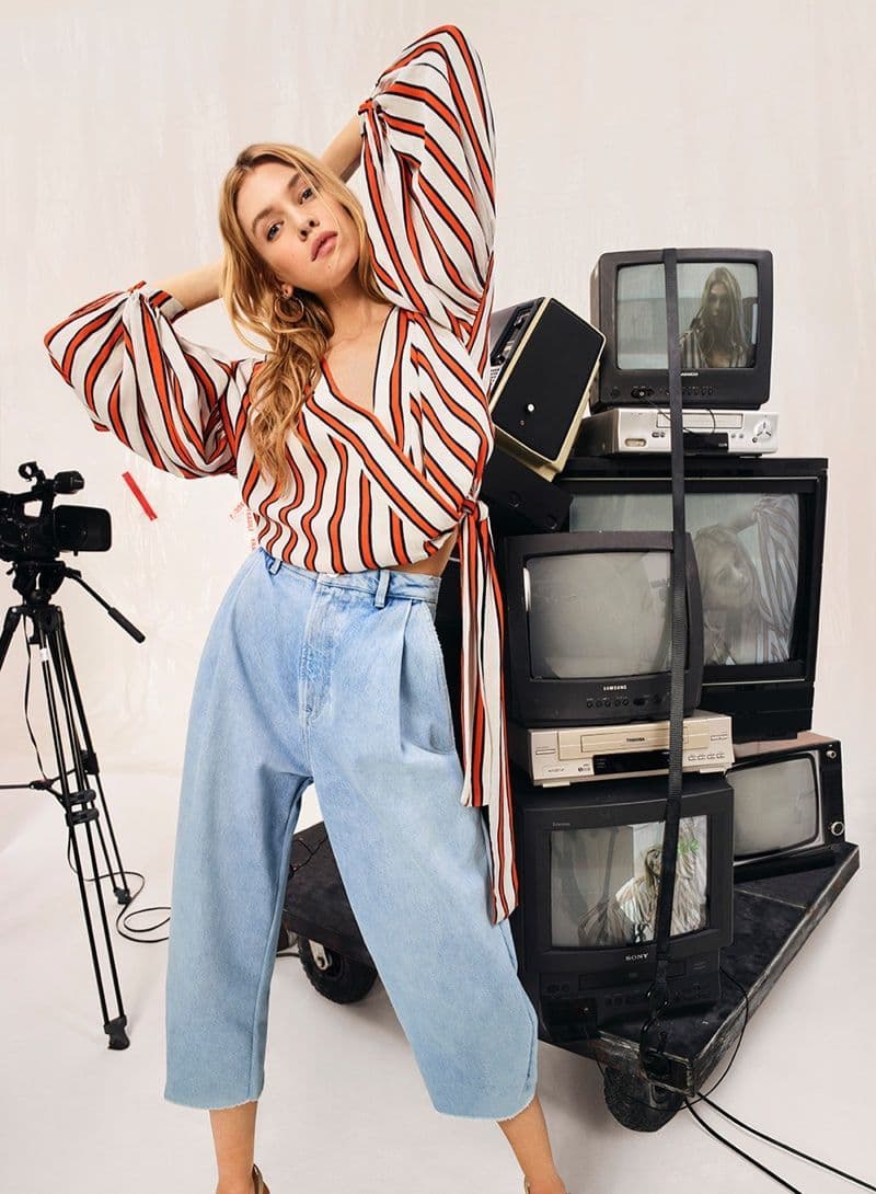 a woman posing in front of a stack of televisions