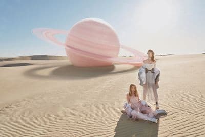 two women sitting in the sand in front of a large object