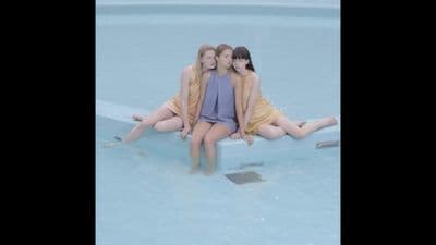 three girls sitting on the edge of a swimming pool