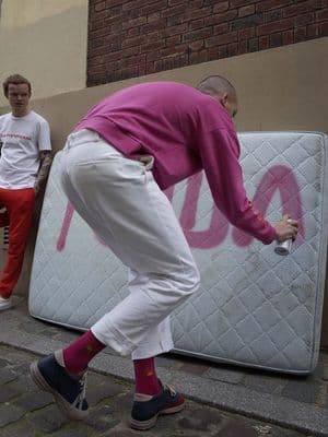 a man in a pink shirt leaning against a mattress