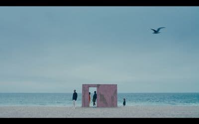three people standing on a beach looking at the ocean