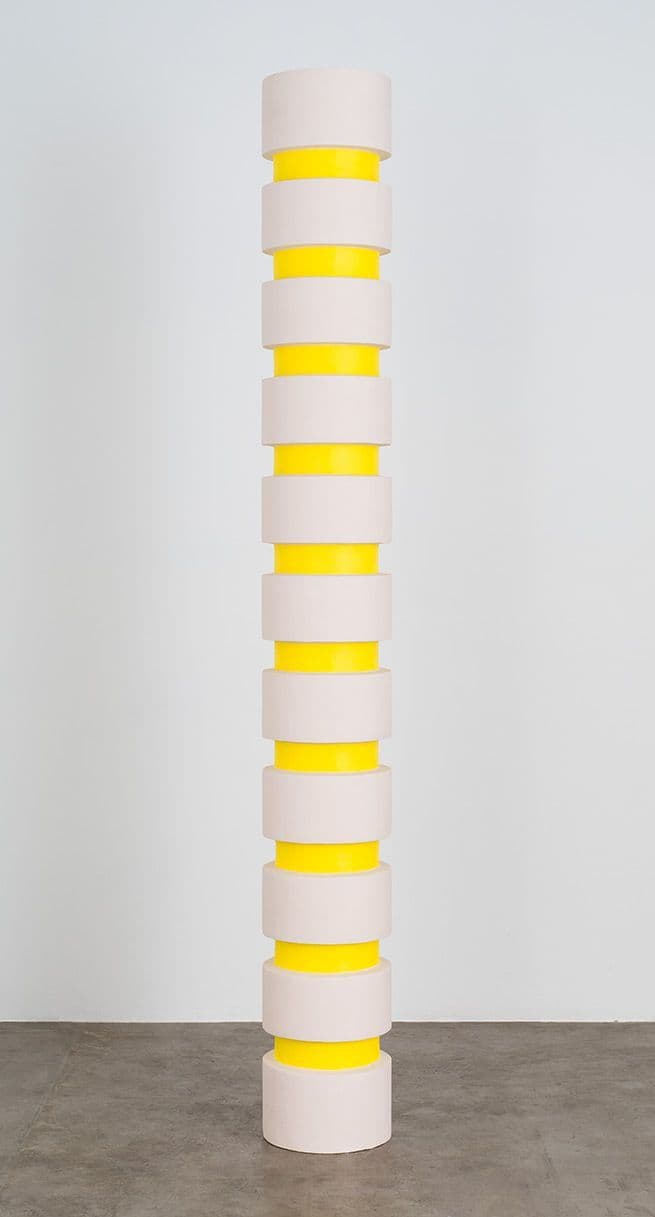 a tall white and yellow vase sitting on top of a cement floor