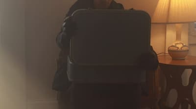 a woman holding a piece of luggage next to a lamp