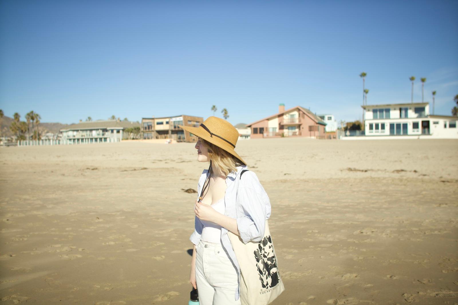 a woman in a hat is walking on the beach