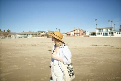 a woman in a hat is walking on the beach