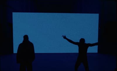 two people standing in front of a large screen