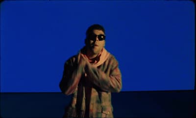 a man wearing sunglasses standing in front of a blue background