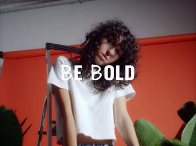a woman standing in front of a red wall with the words be bold