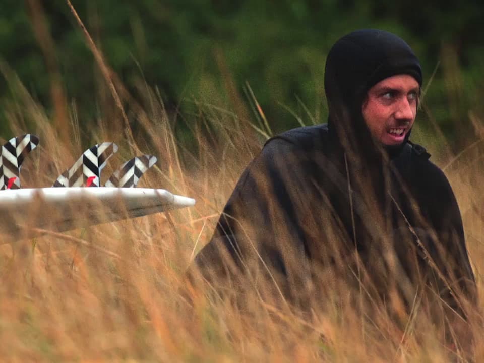 a man in a black hoodie holding a white surfboard