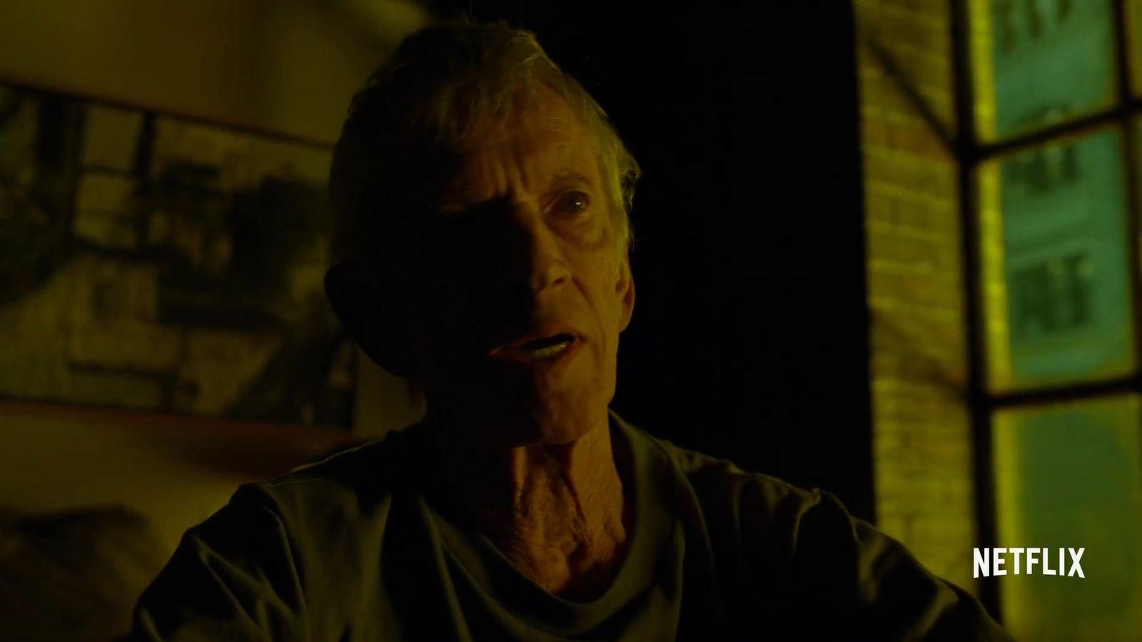 an older man in a dark room looking at the camera