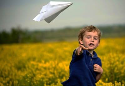 a boy in a field with a paper airplane in the air