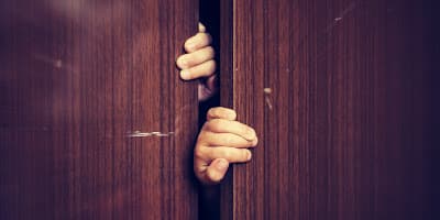 a person's hand peeking through a wooden door