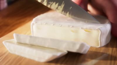 a person cutting a piece of cheese with a knife