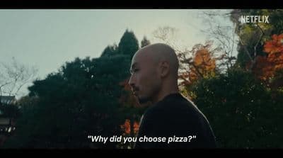 a man with a bald head standing in front of trees