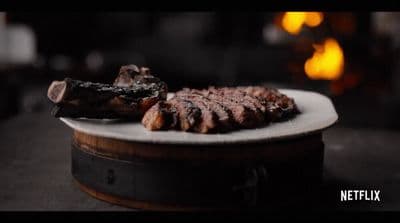 a white plate topped with meat next to a fire