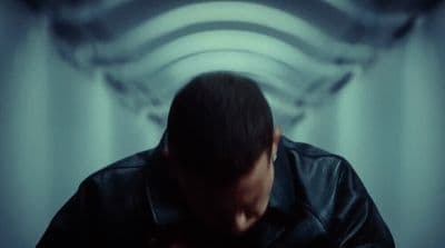 a man in a black leather jacket standing in front of a curtain