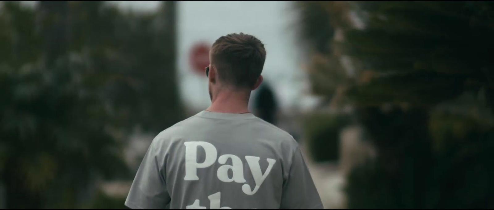 a man walking down a street wearing a shirt that says pay