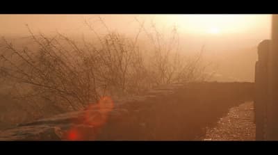 the sun is shining through the fog over a stone wall