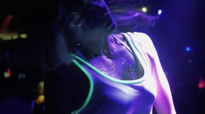 a woman in a neon dress is standing in the dark