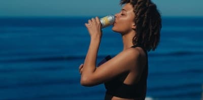 a woman drinking from a bottle near the ocean