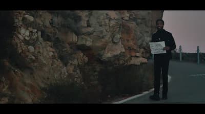 a man standing next to a rock wall holding a sign