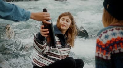 a woman is holding a beer bottle in front of a river