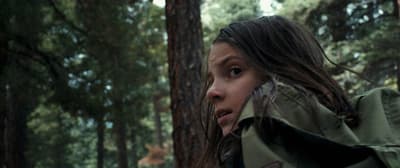 a girl in a green jacket standing in a wooded area