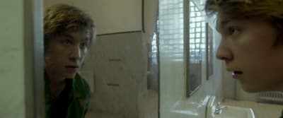 a young man in a green shirt is looking at himself in a mirror