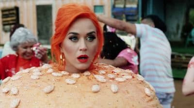 a woman with orange hair and makeup is standing in front of a group of people