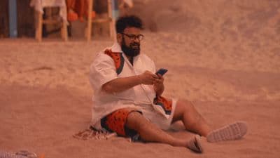 a man sitting in the sand looking at his cell phone