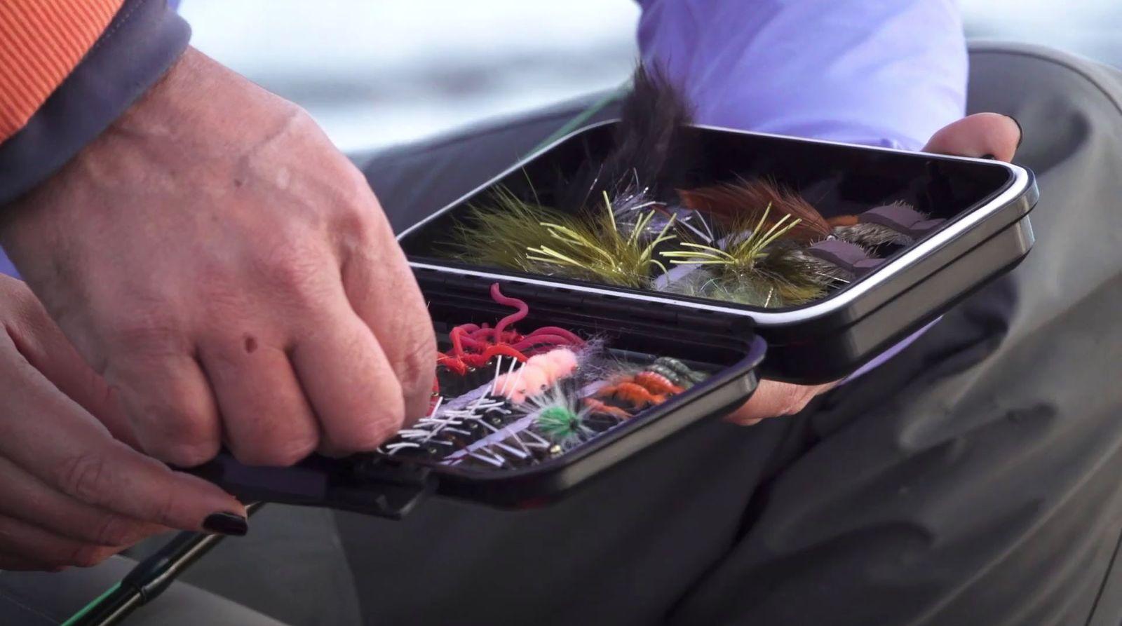 a man holding a fishing box filled with different types of fish