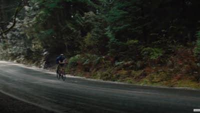 a man riding a bike down a road next to a forest